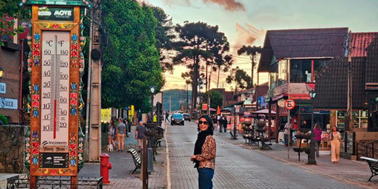 Termômetro instalado em rua de Monte Verde Minas marcando graus em Celsius e turista com roupas de inverno: cachecol, casaco e calça.